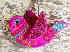 a pink bird ornament hanging from a string on a wooden table with wood planks