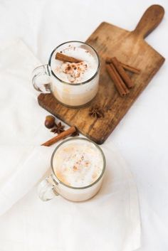 two mugs of hot chocolate with cinnamon on a cutting board