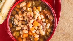 a red bowl filled with beans and carrots next to a sandwich on a table