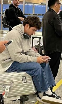 a young man sitting on top of an airport luggage bag while looking at his cell phone