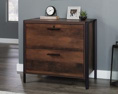 a wooden cabinet with two drawers and a clock on it's top, against a gray wall