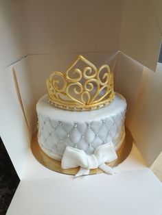 a white and gold cake with a tiara on top in a box that is open