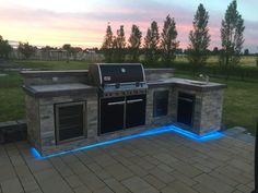 an outdoor kitchen with blue lights on the side and brick flooring in front of it