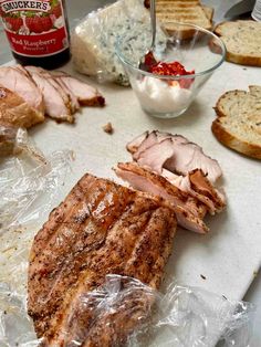 some meat and bread on a cutting board with plastic wrapper around the edges, ready to be cooked