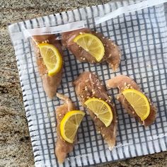 four pieces of fish with lemon slices on a towel in the middle of a granite countertop