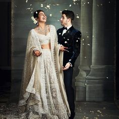 a man and woman standing next to each other in front of an arch with petals falling from it