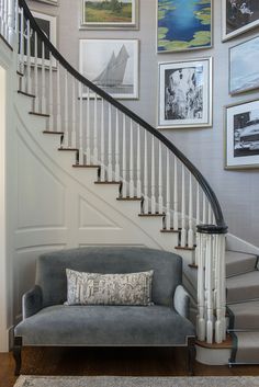 a grey couch sitting under a stair case next to a white bannister with pictures on the wall