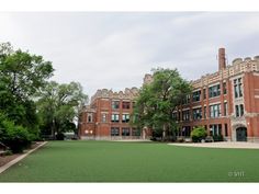 an old brick building with green grass in the foreground and trees on either side