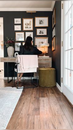 a woman sitting at a desk in front of some pictures on the wall and floor