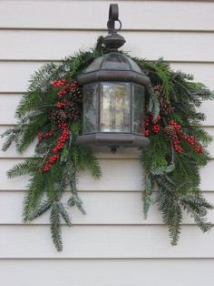 a christmas wreath hanging from the side of a house with pine cones and red berries