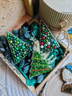 three christmas trees in a wooden box on a table next to other ornaments and decorations