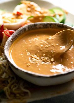 a bowl of soup with a spoon in it on a plate next to some vegetables