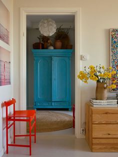 a blue cabinet sitting in the corner of a room next to a red chair and yellow flowers