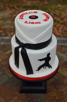 a white cake with black ribbon and red lettering on the top is sitting on a stand