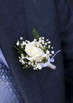 a boutonniere with white flowers and greenery attached to the lapel