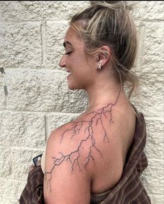 a woman with a lightning tattoo on her upper arm and shoulder, standing in front of a white brick wall