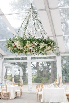 a chandelier filled with flowers and greenery hangs from the ceiling at a wedding reception