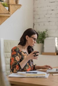 a woman sitting at a desk using a laptop computer while holding a cup of coffee