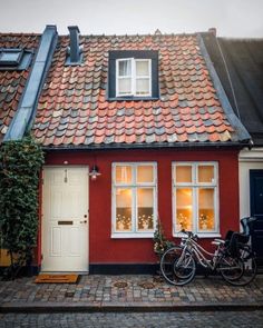 a bicycle parked in front of a red house with two windows and a tiled roof