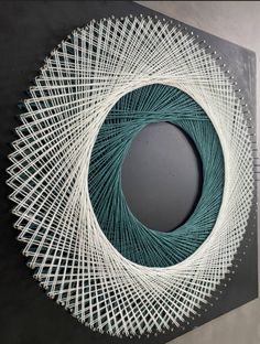 a white and green string art piece hanging on the wall next to a round mirror