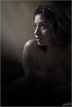 a naked woman sitting in the dark with her head turned to the side and looking off into the distance