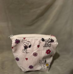 a small white pouch with snoopy dogs and flowers all over it, on a gray background