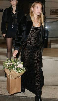 a woman in a long black dress carrying flowers