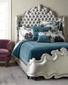 a bed with blue and white pillows in a bedroom next to a purple velvet chair