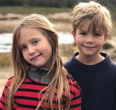 two young children standing next to each other in front of a body of water and trees