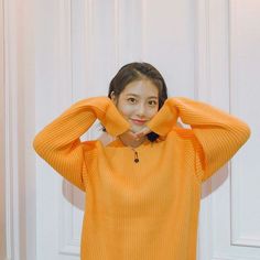 a woman in an orange sweater poses for the camera with her hands on her head