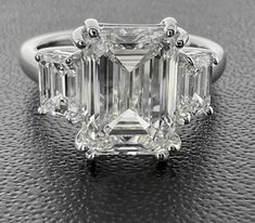 an emerald - cut diamond ring with three baguets on the sides and four clawed shoulders