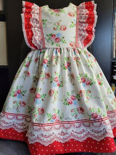 Baby frock dress, with gather skirt and wide band of red polka dots at hem. Bodice with round neck and lateral ruffles band from back to front, covering parts of the armholes from half part of shoulders. These ruffles are in the polka dots also. Laces are covering part of skirt band and the bodice ruffles. A narrow taffeta ribbon is sewn at the junction of this parts to dress main parts. Sleeveless Polka Dot Dress With Lace Trim, Red Fitted Dress With Ruffled Straps, Red Sleeveless Dress With Lace Trim, Vintage Ruffle Dress With Flutter Sleeves, Vintage Flutter Sleeve Dress With Ruffles, Vintage Dresses With Ruffles And Flutter Sleeves, Red Floral Dress With Ruffles For Garden Party, Vintage Red Dress For Garden Party, Red Vintage Dress With Lace Trim