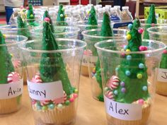 cupcakes decorated like christmas trees with name tags and candy on them sitting in plastic cups