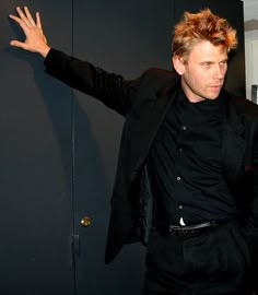 a man in a black shirt and suit with his arms out, standing next to a door