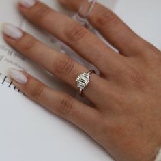 a close up of a person's hand with a ring on their finger and an open book in the background