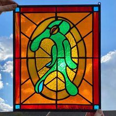 a person holding up a stained glass window in front of a blue sky with clouds