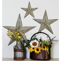 three metal stars on the wall with flowers in buckets and watering can next to them