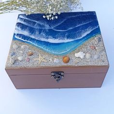 a wooden box with sand and shells on the bottom, along with seashells