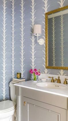 a bathroom with blue and white wallpaper, gold framed mirror, toilet and sink