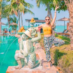 a woman standing next to a fountain with a monkey on it's head and arms in the air