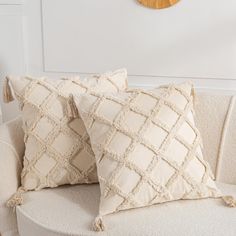 two decorative pillows on a white couch in front of a wall with a wooden clock