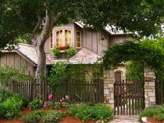 a house with flowers in the window boxes on the front and side of it, surrounded by greenery