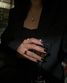 a woman holding a wine glass in her right hand and wearing gold rings on her left wrist