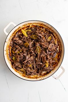 a pot filled with shredded beef and peppers on top of a table next to a fork