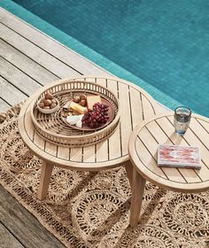 two wooden tables sitting on top of a rug next to a swimming pool with food