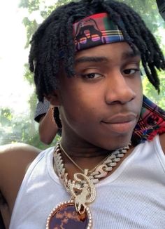 a man with dreadlocks wearing a white tank top and a necklace on his neck