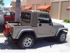 a gray jeep parked in front of a building next to a red truck and palm tree