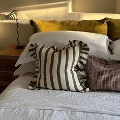 a bed topped with lots of pillows next to a lamp