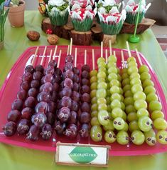 grapes and olives are arranged on sticks for sale at an outdoor buffet table with cupcakes in the background