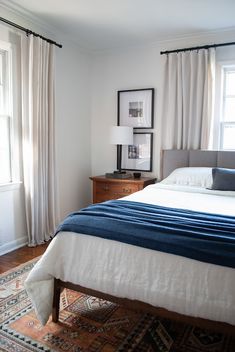 a bedroom with a large bed and two windows in the corner, along with a rug on the floor